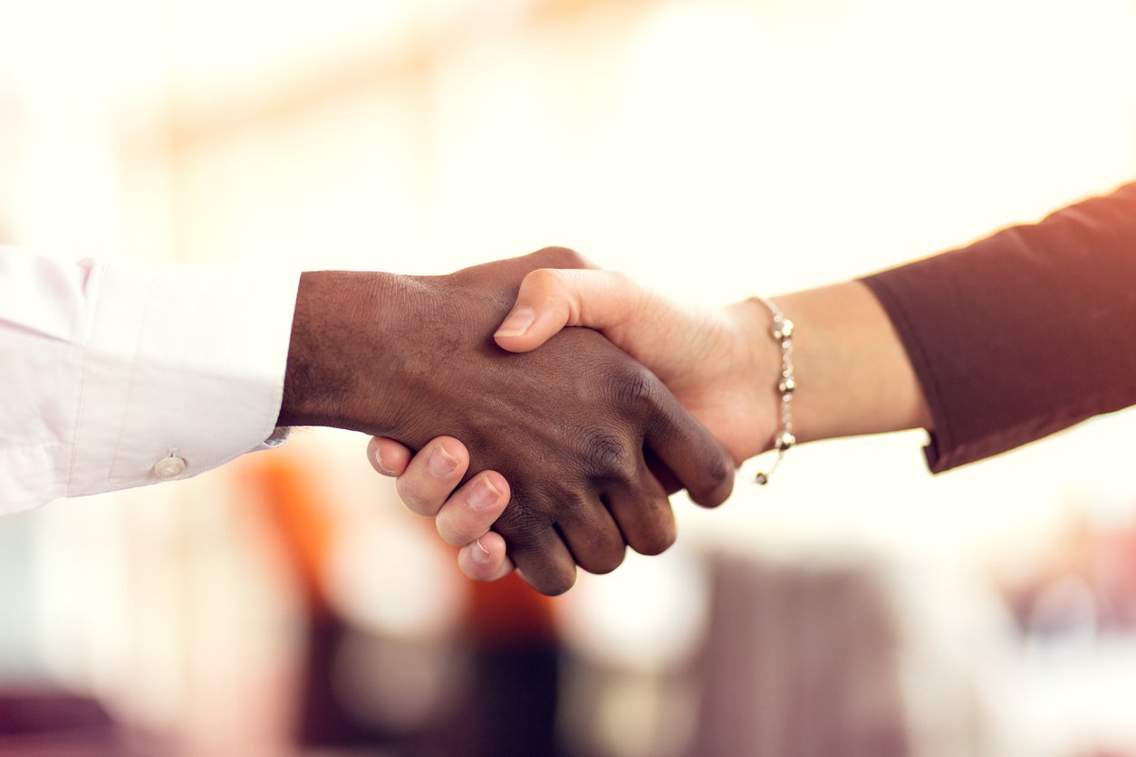 A Black business man and a white, business woman shaking hands in agreement